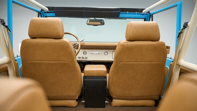 Front seats and dashboard area of Classic Ford Bronco with tan leather upholstery and roll cage