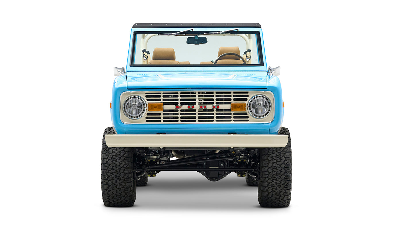 Front view of Classic Ford Bronco in bright blue showing grille, headlights, and beige bumper