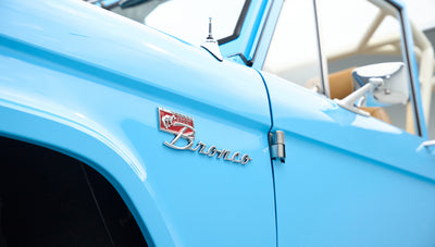 Side view of bright blue Classic Ford Bronco showing front fender emblem and rearview mirror