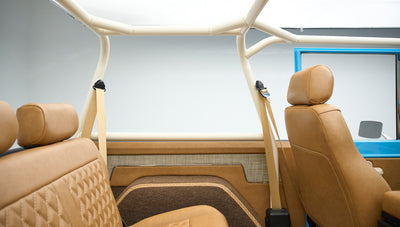 Interior view showing front and rear brown leather seats with roll cage and tan seatbelts