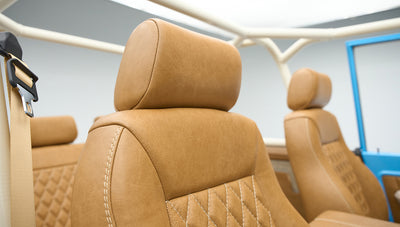Tan leather front seats with headrests inside a Classic Ford Bronco with roll cage and blue door frame