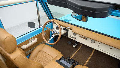 Driver's seat and dashboard of Classic Ford Bronco with tan leather seats and blue exterior visible