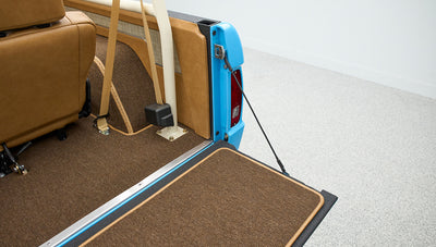 Open tailgate and rear cargo area of Classic Ford Bronco showing tan upholstery and beige seat belts