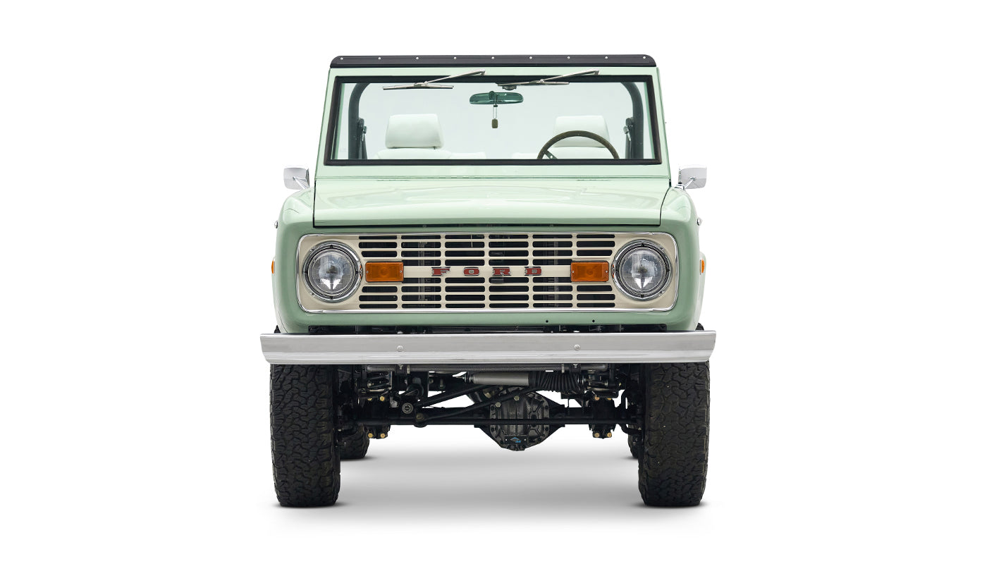 Front view of a mint green Classic Ford Bronco with white interior and black roof