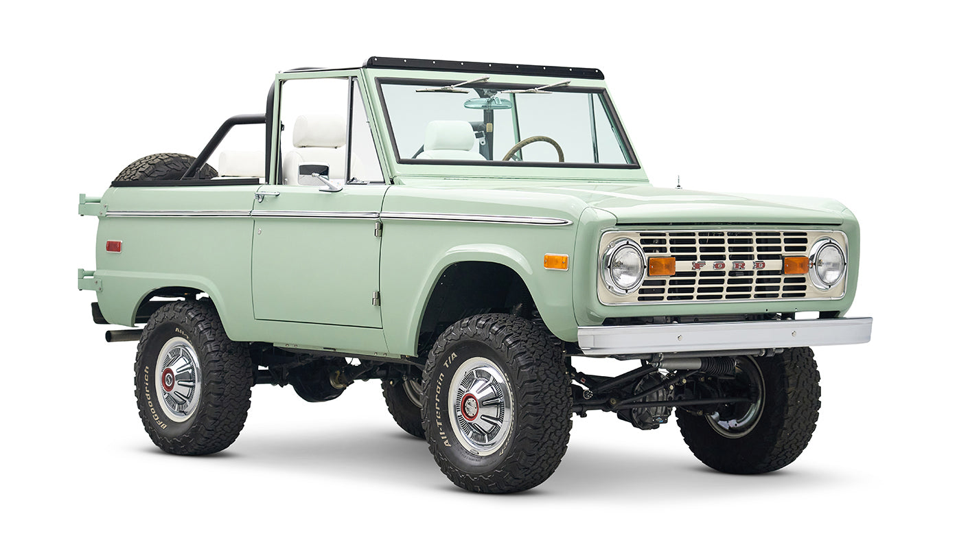 Classic Ford Bronco in pale green with white interior and black roll bar, three quarter front view slightly tilted