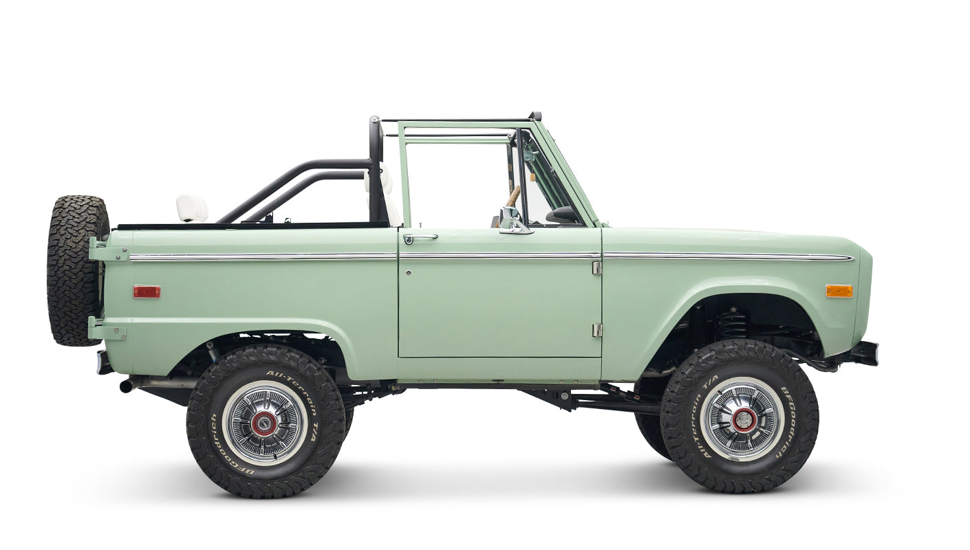 Classic Ford Bronco in pale green with white interior and black roll bar, side view without doors