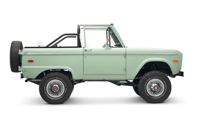 Classic Ford Bronco in pale green with white interior and black roll bar, side view without doors