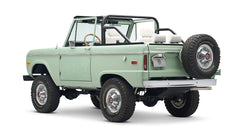 Classic Ford Bronco in pale green with white interior and black roll bar, three quarter rear view showing spare tire