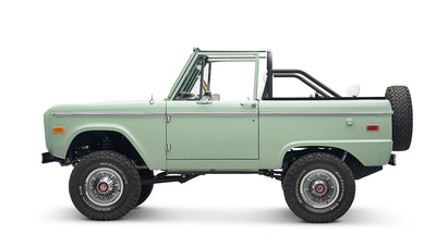 Classic Ford Bronco in pale green with white interior and black roll bar, side view with spare tire on rear