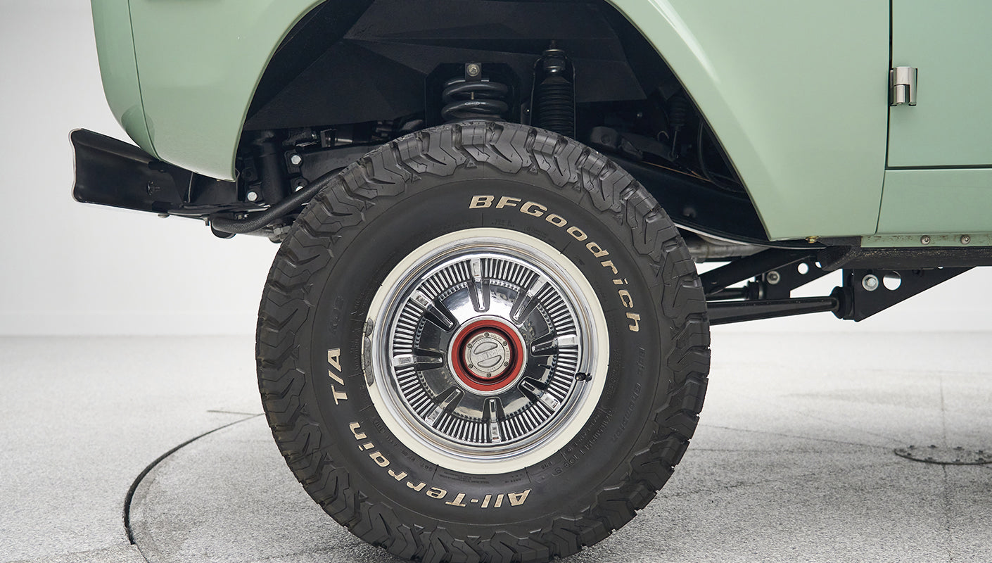 Side view of front tire and suspension underneath mint green Classic Ford Bronco