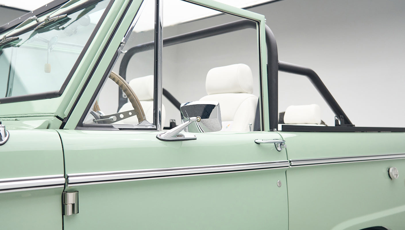 Open driver side door showing black side mirror and white seats inside Classic Ford Bronco