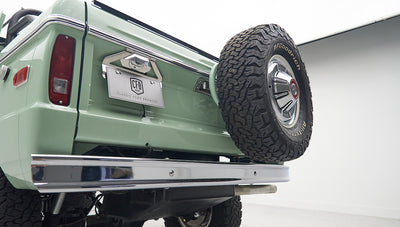 Back angle of green Classic Ford Bronco showing rear bumper and mounted spare tire