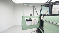 Open driver door of green Classic Ford Bronco showing interior upholstery and steering wheel