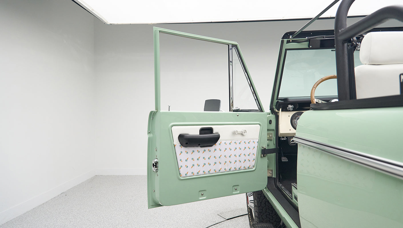 Open driver door of green Classic Ford Bronco showing interior upholstery and steering wheel