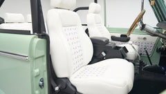 Close-up of two white front seats with pineapple pattern and wooden steering wheel inside Classic Ford Bronco