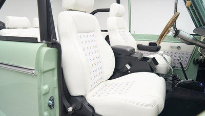 Close-up of two white front seats with pineapple pattern and wooden steering wheel inside Classic Ford Bronco