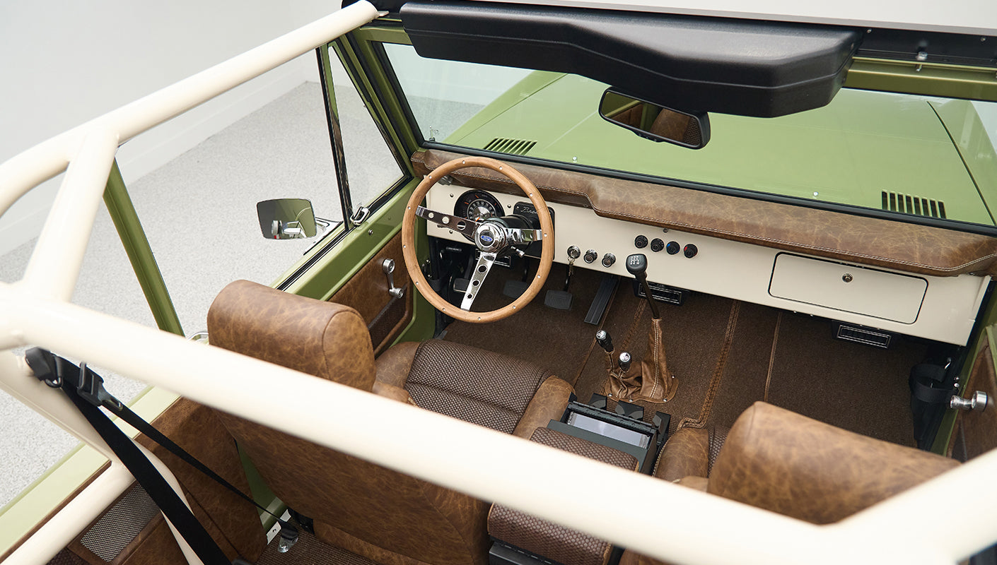 Overhead view into Classic Ford Bronco showing steering wheel, gear shifts, and brown seats