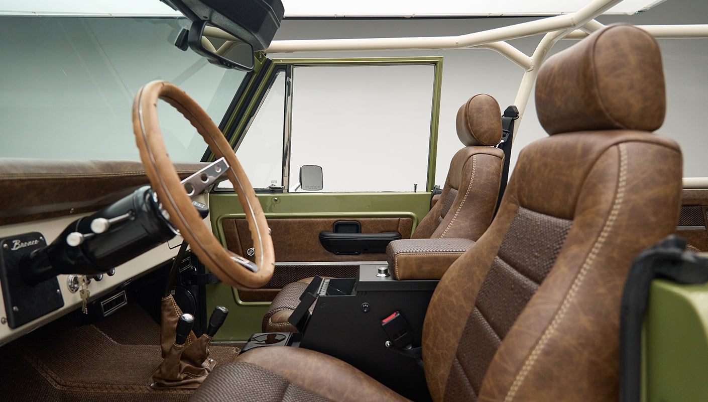 Angle view of front seats inside Classic Ford Bronco Lime Gold showing brown upholstery and steering wheel