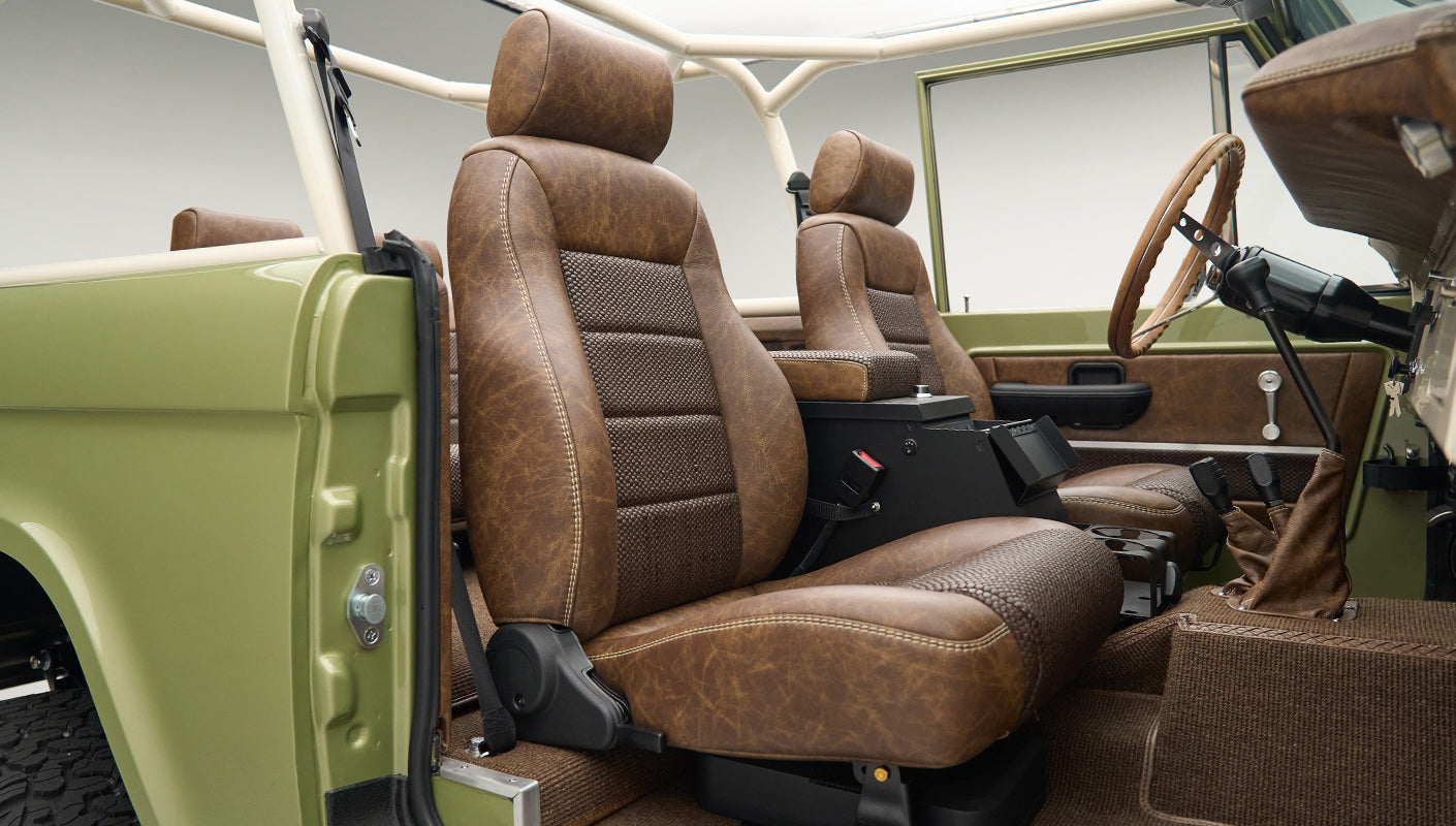 Interior side view of open door with vintage brown leather driver and passenger seats in Classic Ford Bronco