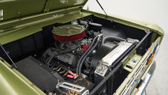 Classic Ford Bronco engine bay showing engine, air filter, radiator, and battery in light green body paint