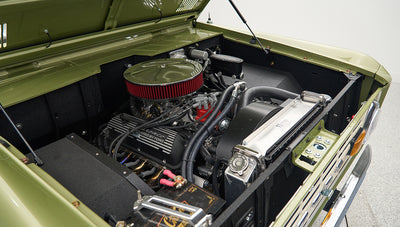Classic Ford Bronco engine bay showing engine, air filter, radiator, and battery in light green body paint