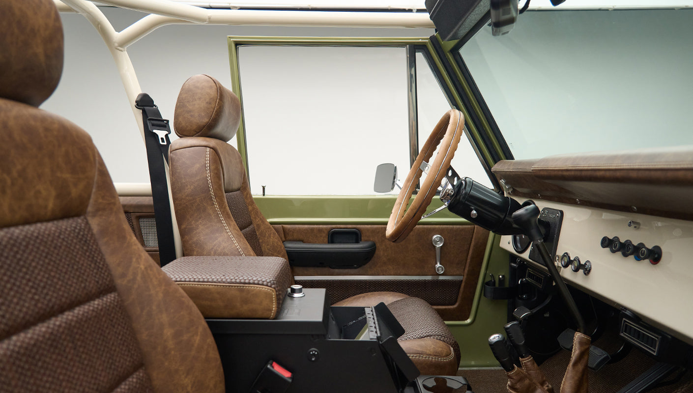 Side view of front cabin with steering wheel, dashboard, and brown leather seats in Classic Ford Bronco Lime Gold