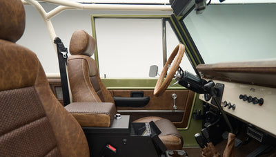 Side view of front cabin with steering wheel, dashboard, and brown leather seats in Classic Ford Bronco Lime Gold