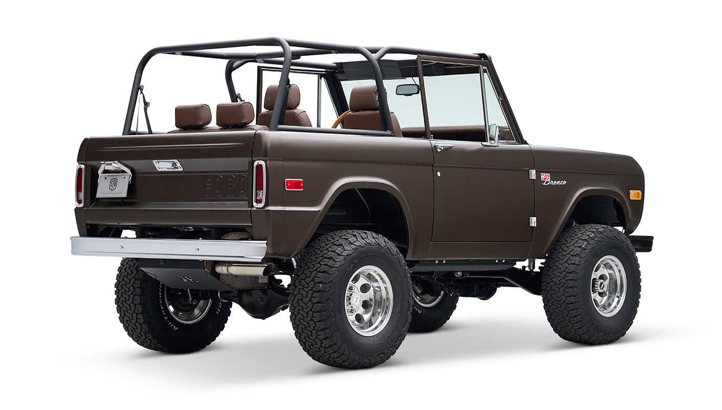 Classic Ford Bronco in matte brown with open roof and brown leather seats, rear angled view