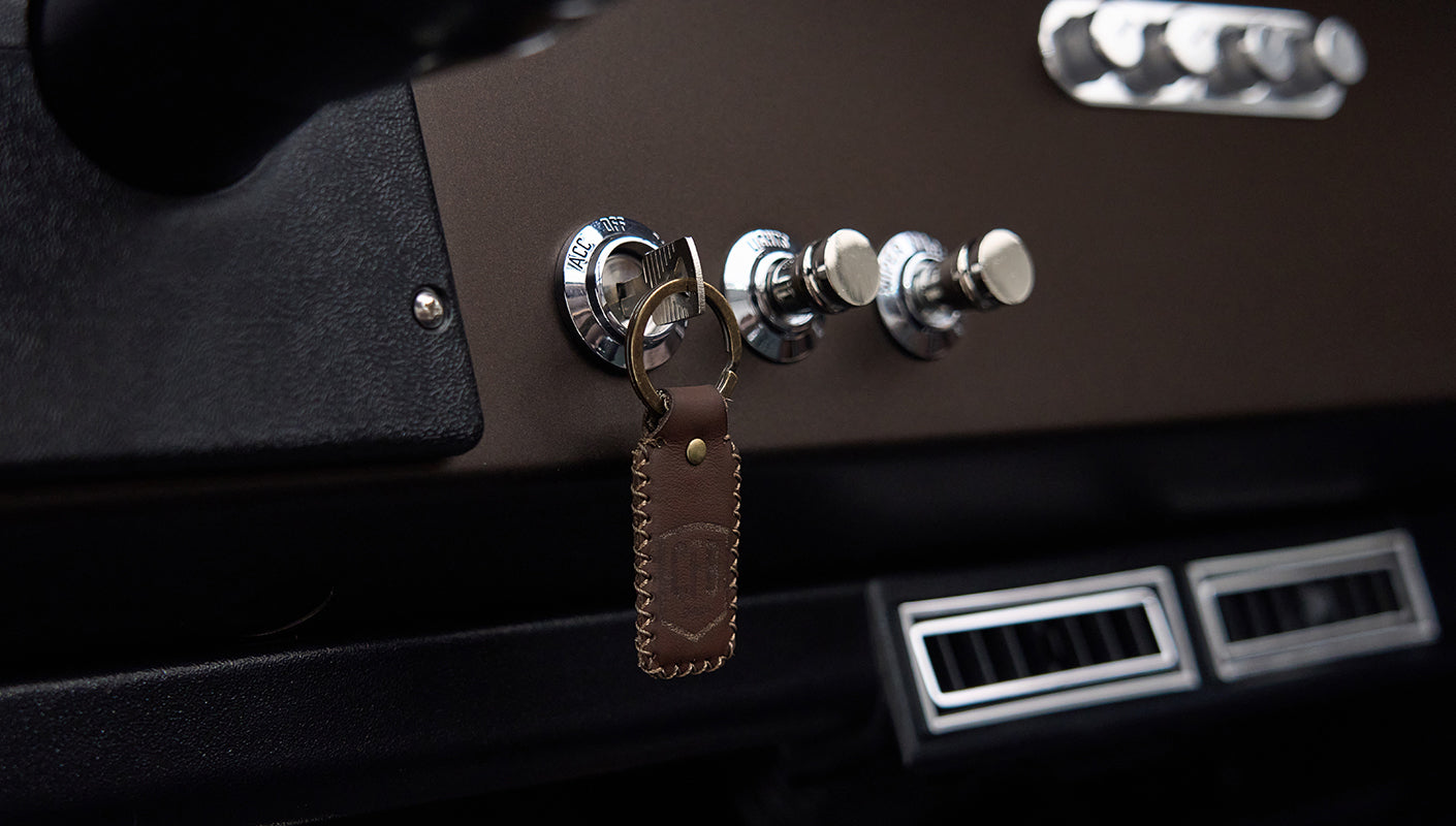 Close-up of ignition switch with key and chrome knobs on brown dashboard in Classic Ford Bronco