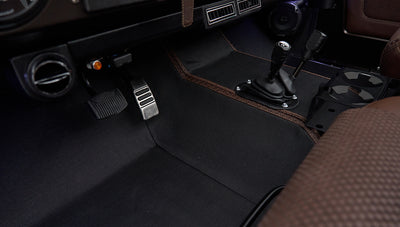 Floor pedals and gearshift area with brown and black floor mats inside Classic Ford Bronco
