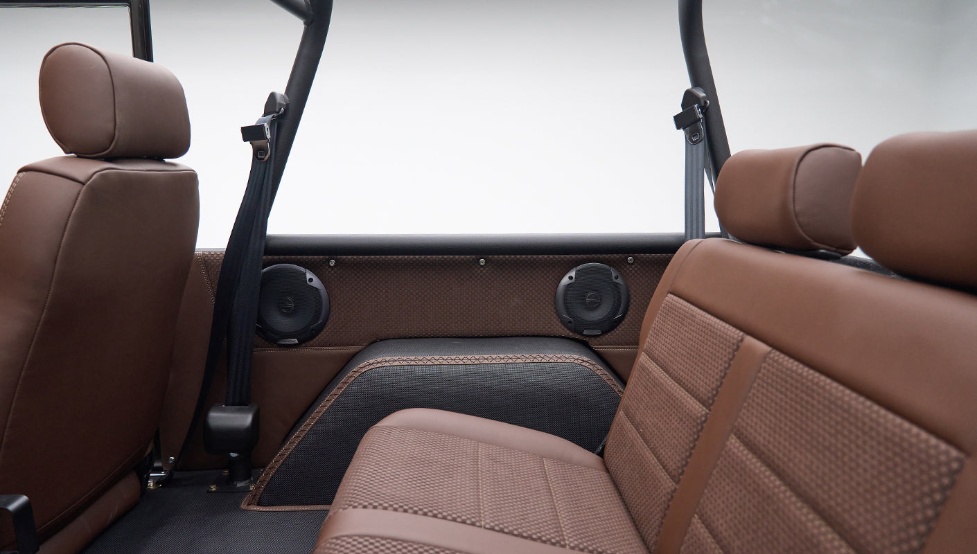 Back seat area showing side panels with speakers and seat belts inside matte brown Classic Ford Bronco