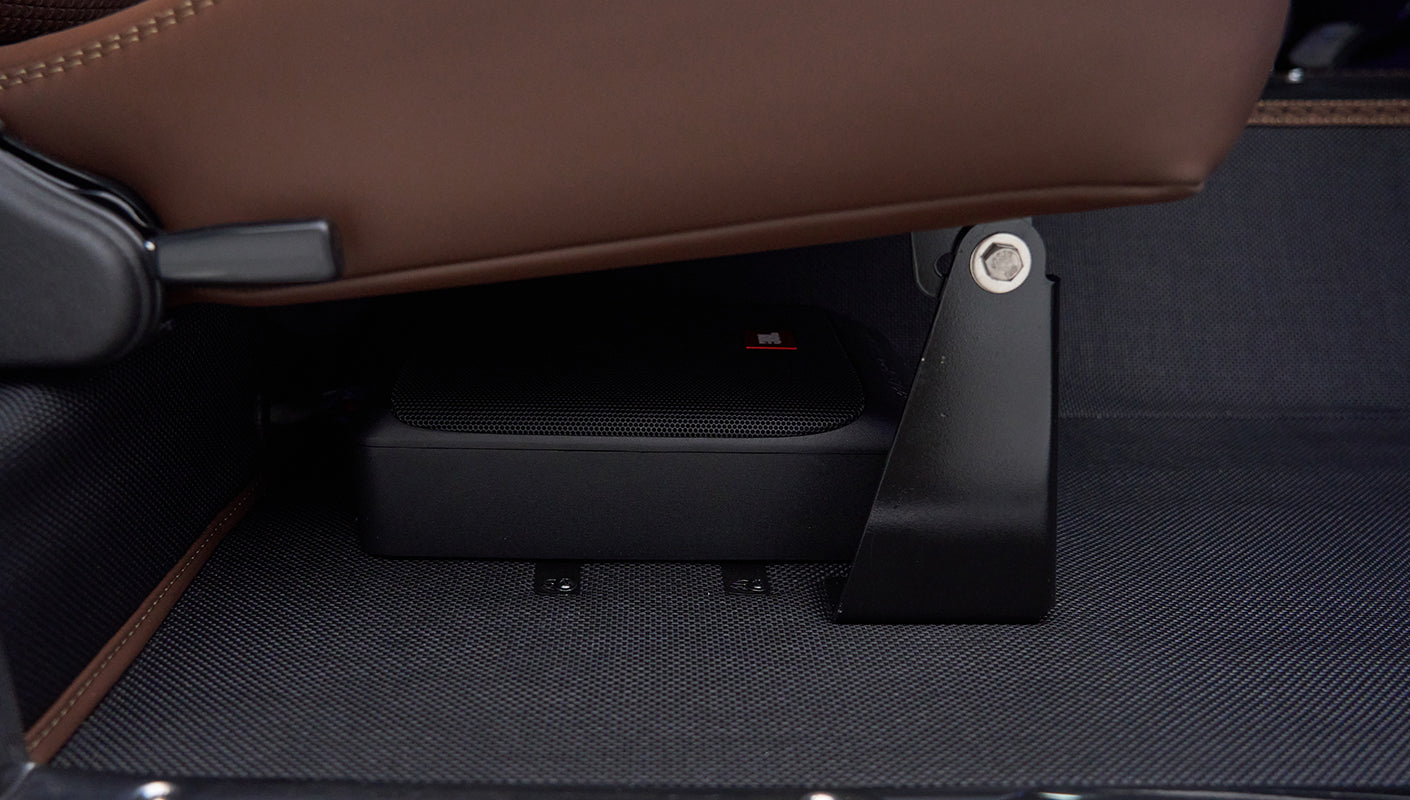 Speaker installed under front seat bracket on textured floor mat inside Classic Ford Bronco