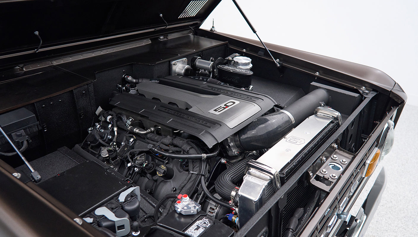 Under hood view showing 5.0 engine and components of Classic Ford Bronco in matte brown