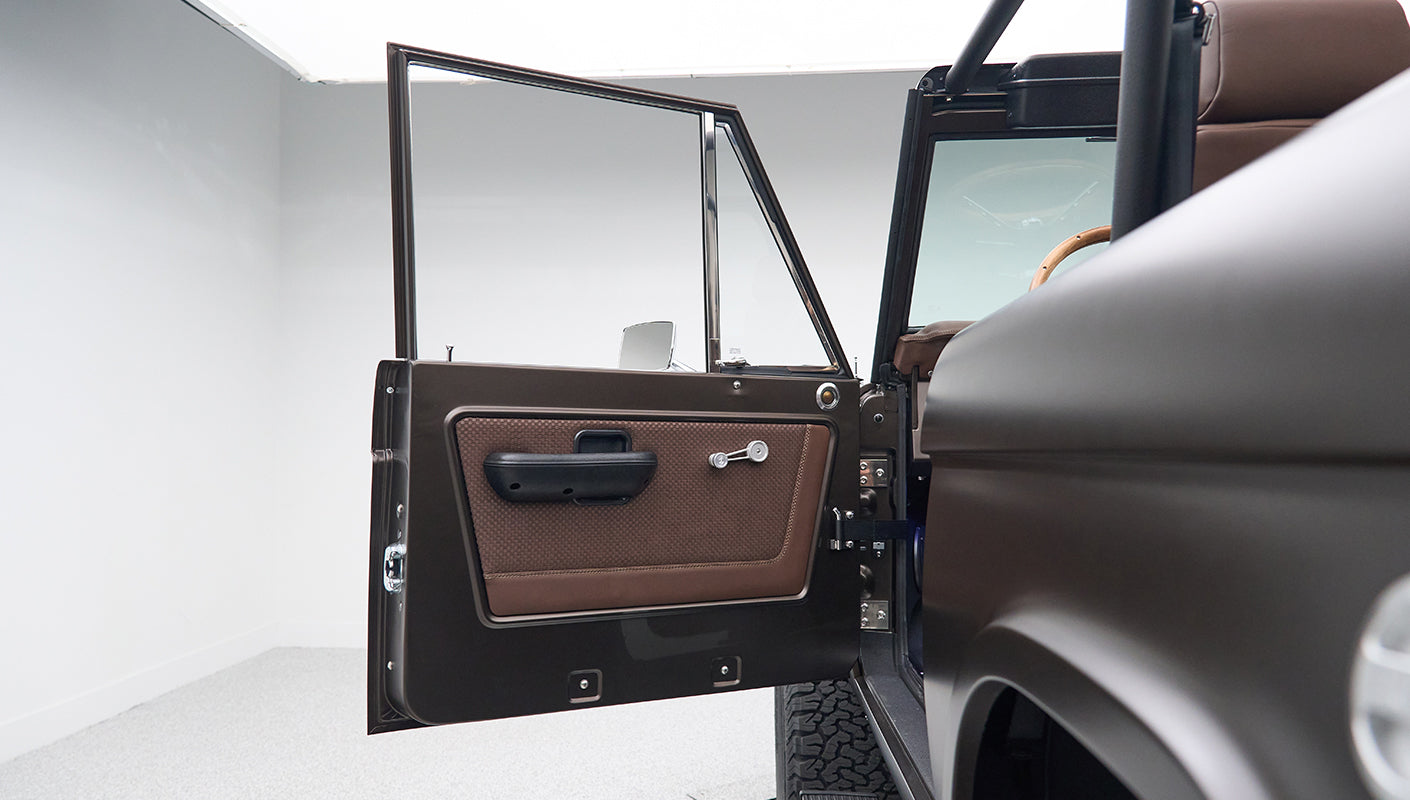 Open driver side door of Classic Ford Bronco showing brown door panel and window crank