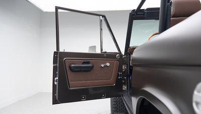 Open driver side door of Classic Ford Bronco showing brown door panel and window crank