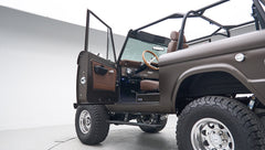 Classic Ford Bronco with driver door open showing side body, brown interior, and wood steering wheel