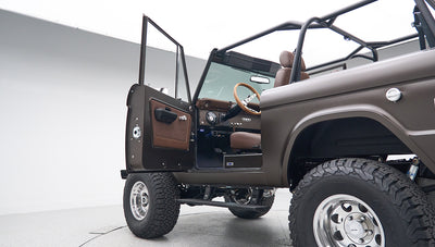 Classic Ford Bronco with driver door open showing side body, brown interior, and wood steering wheel