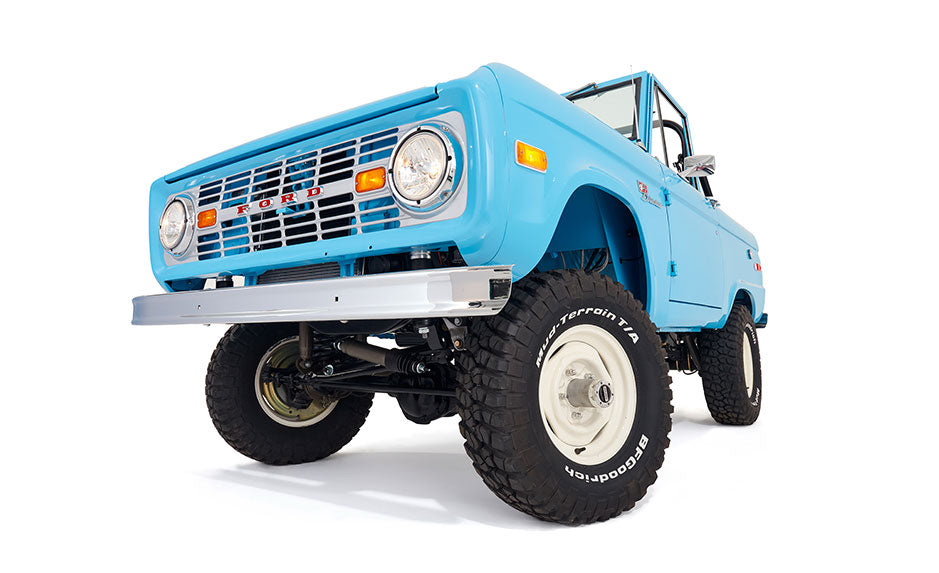Light blue Classic Ford Bronco angled front view with large tires against white background