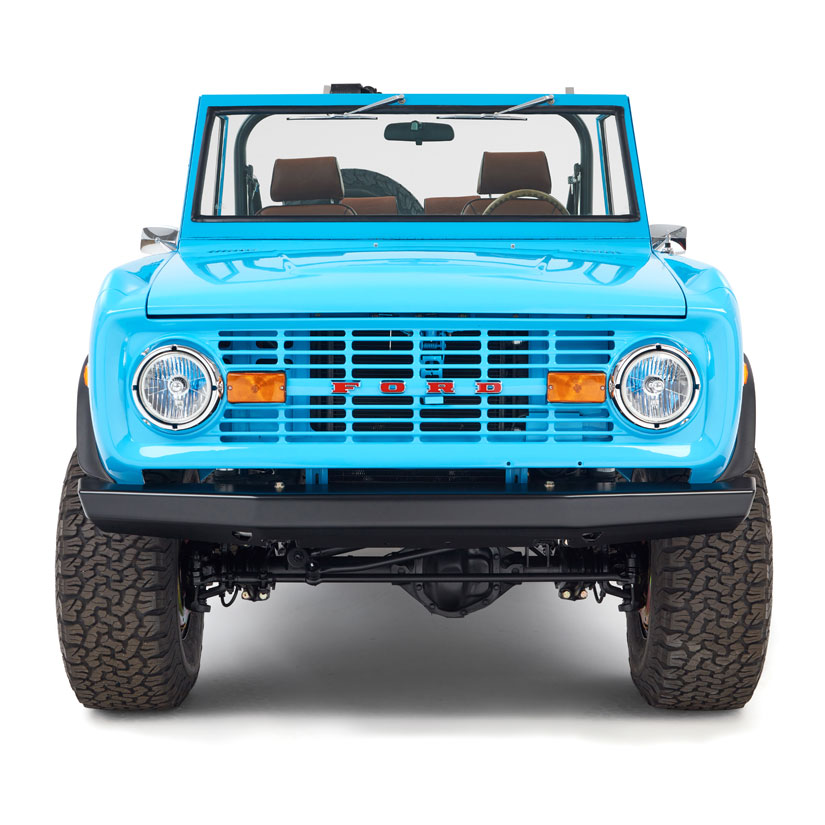 Front view of a bright blue Classic Ford Bronco with windshield and brown seats