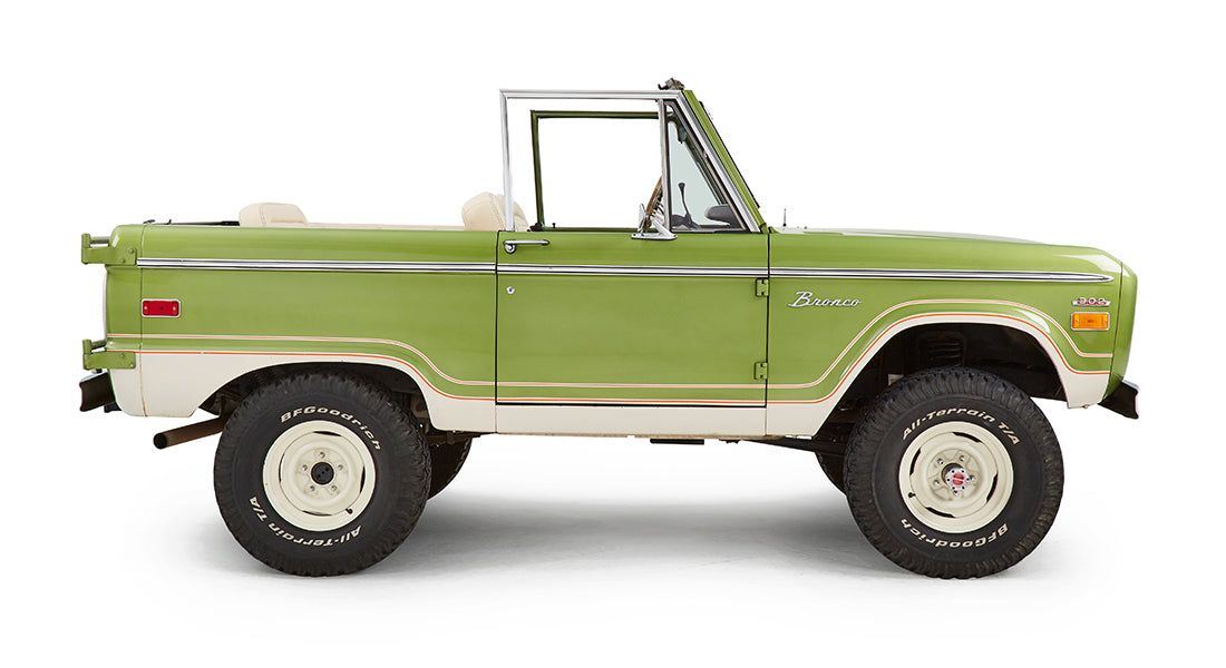 Side profile of green Classic Ford Bronco with open roof and beige seats