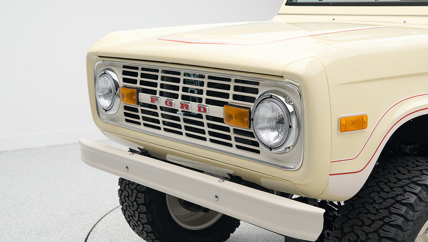 Close-up of front grille and headlights of pale yellow Classic Ford Bronco with red pinstripe