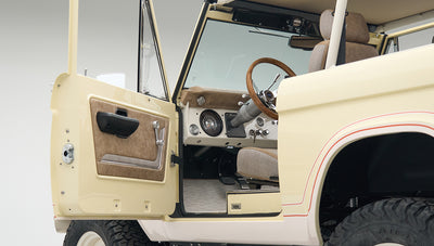 Open driver door showing tan and fabric interior, steering wheel and dashboard of Classic Ford Bronco