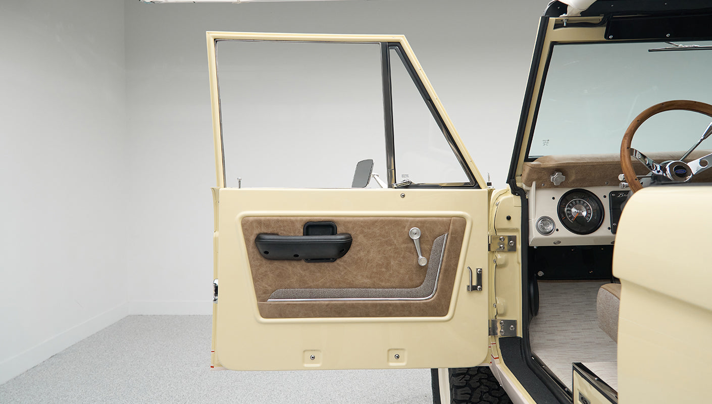 Open driver door of Classic Ford Bronco showing beige and brown door panel and part of the dashboard
