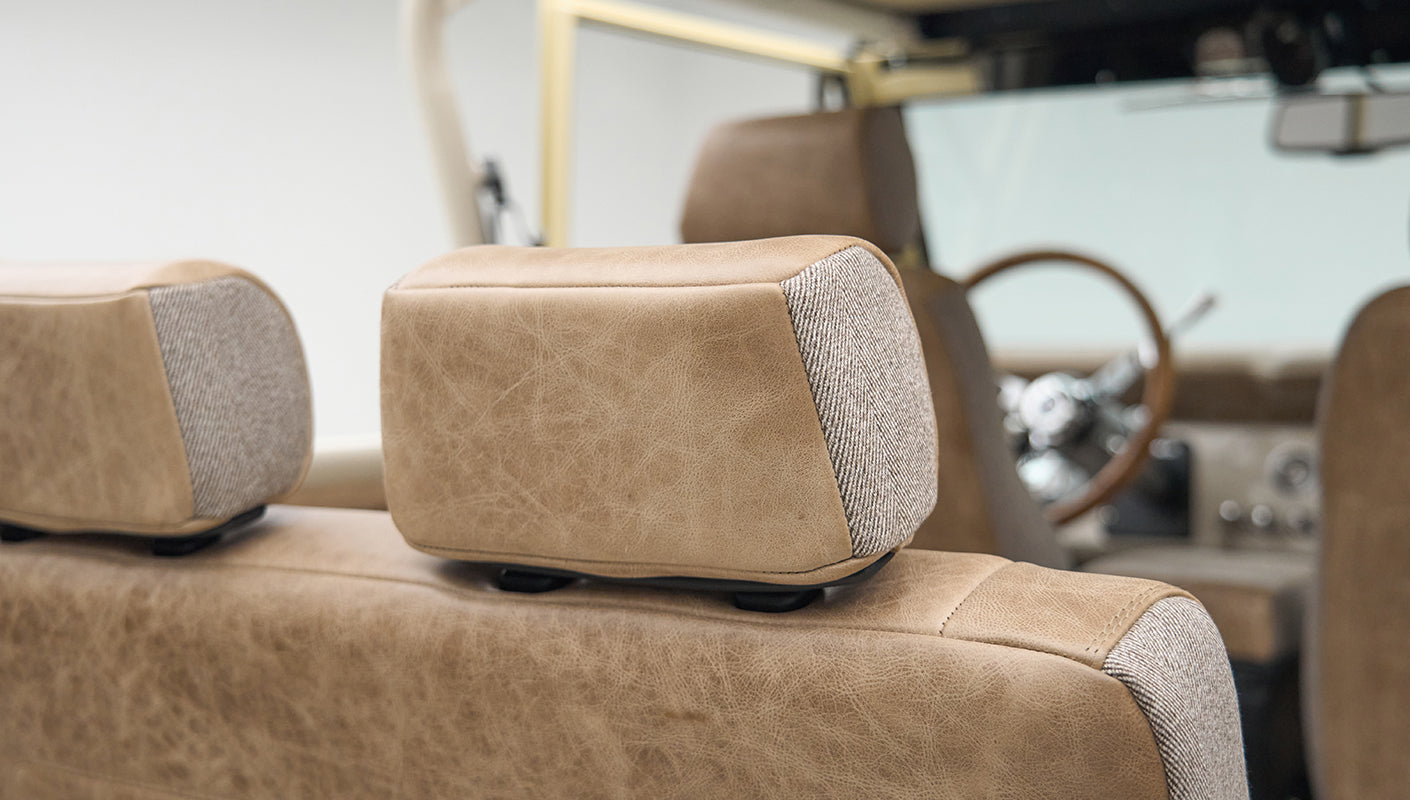 Headrest of beige leather and fabric seat in Classic Ford Bronco with steering wheel in background