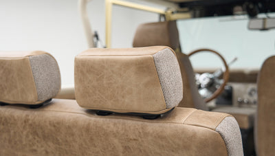 Headrest of beige leather and fabric seat in Classic Ford Bronco with steering wheel in background
