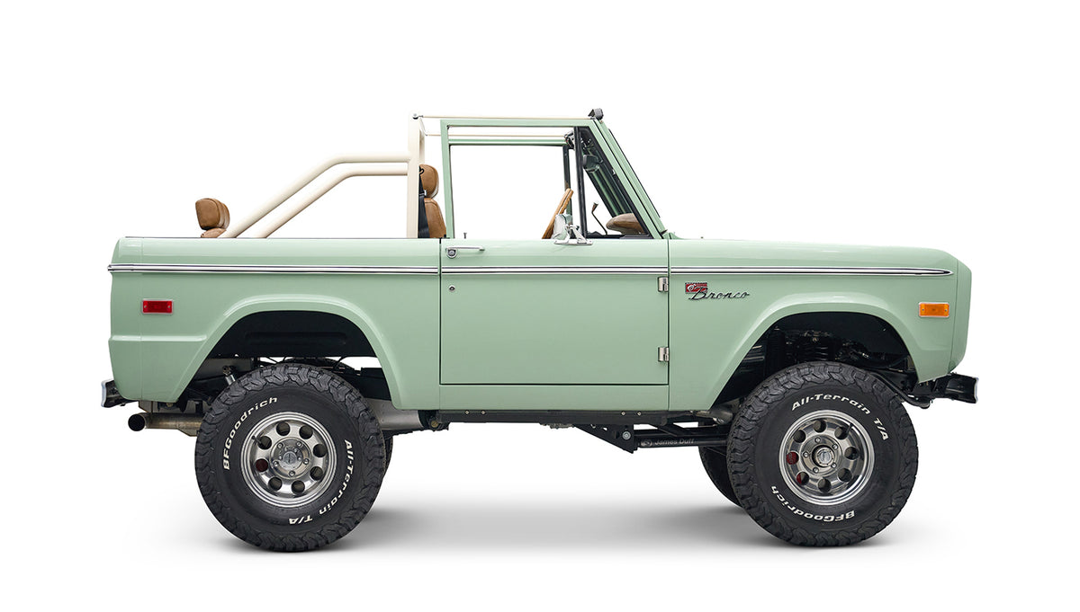 Side view of porcelain green Classic Ford Bronco with tan interior and white roll cage