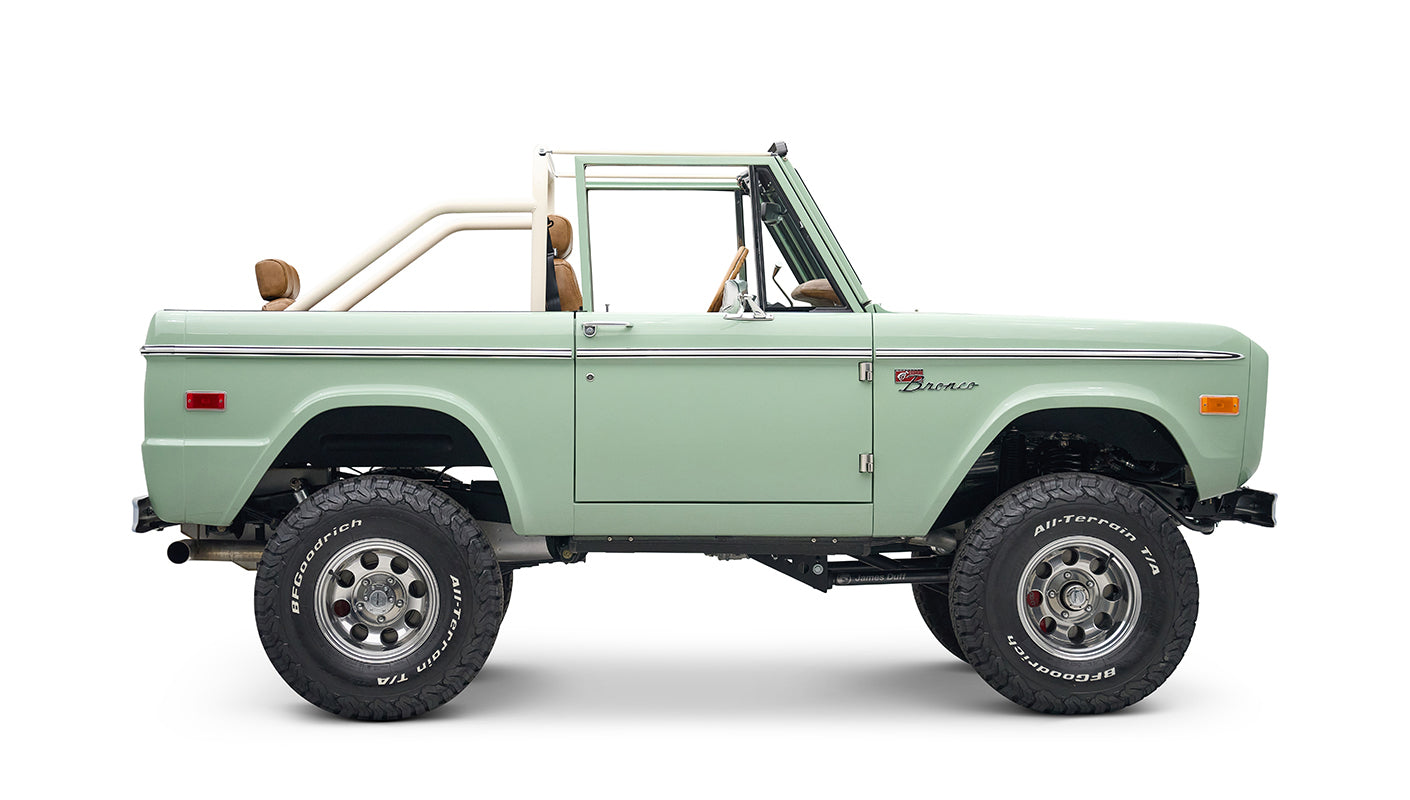 Side view of porcelain green Classic Ford Bronco with tan interior and white roll cage