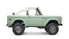 Side view of porcelain green Classic Ford Bronco with tan interior and white roll cage