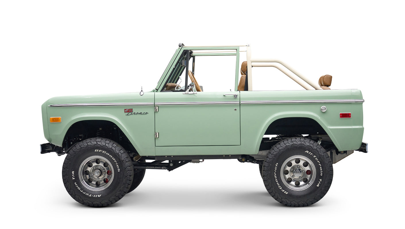 Side view of a porcelain green Classic Ford Bronco with white roll cage and off-road tires
