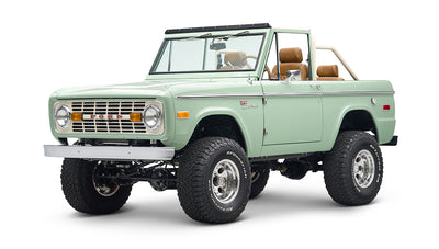 Front and side view of green Classic Ford Bronco convertible with chrome wheels and black soft top frame